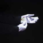 magician-removing-aces-playing-card-from-hand-against-black-background-scaled